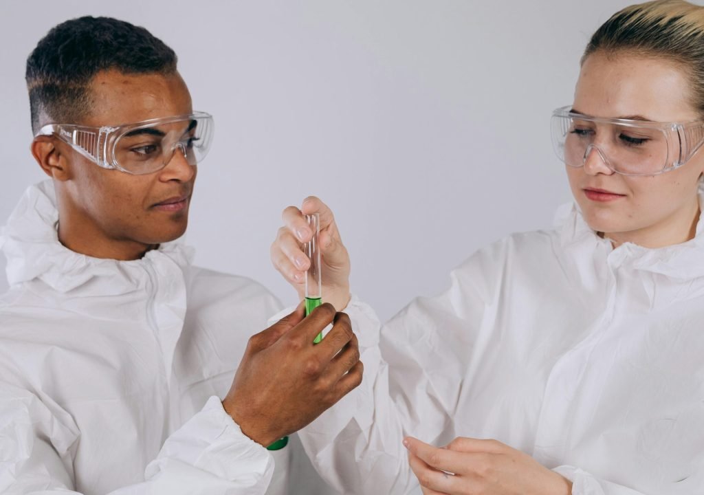 Two scientists in protective gear working together in a lab setting.